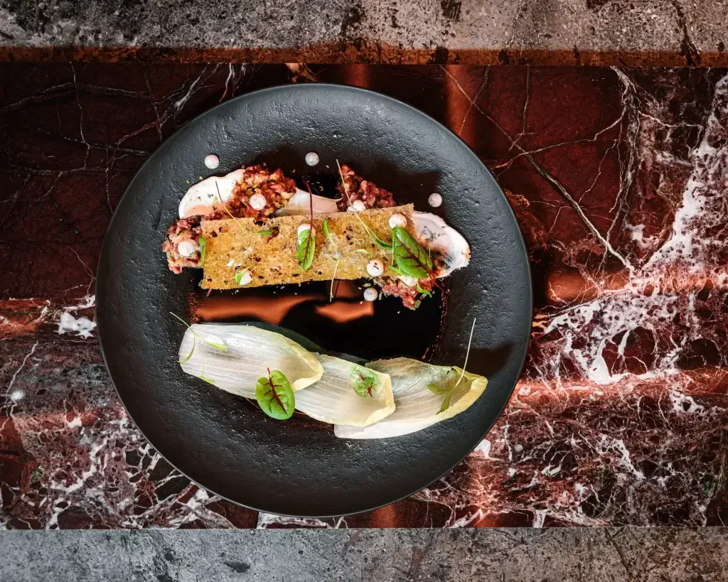 Exquisite Plated Dish at Animl A gourmet dish presented on a black plate, garnished with fresh herbs and sauces, served at Animl Steakhouse.