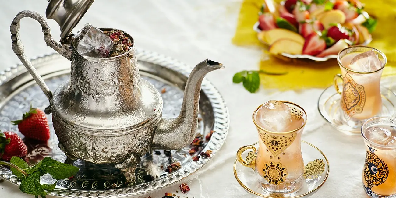 Byblos Moroccan Tea Experience A traditional Moroccan tea service at Byblos, featuring an ornate silver teapot, gold-patterned tea glasses, and fresh fruit on an elegant tray.